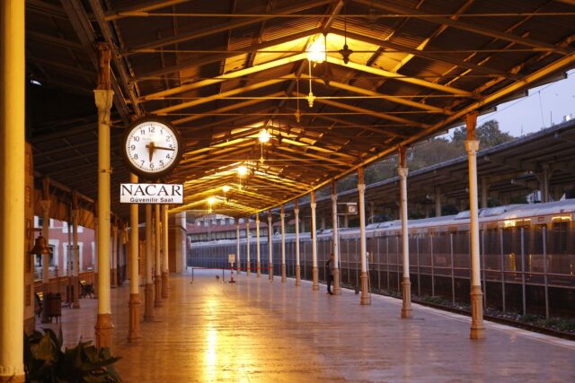 Un peron de gară aproape gol, la lăsarea serii, cu o linie de tren care se pierde în depărtare